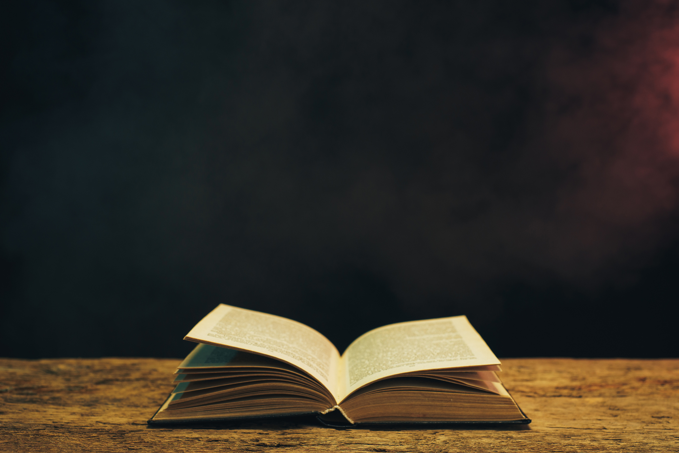 Old book on a oak wooden table. Background of blue and red smoke.